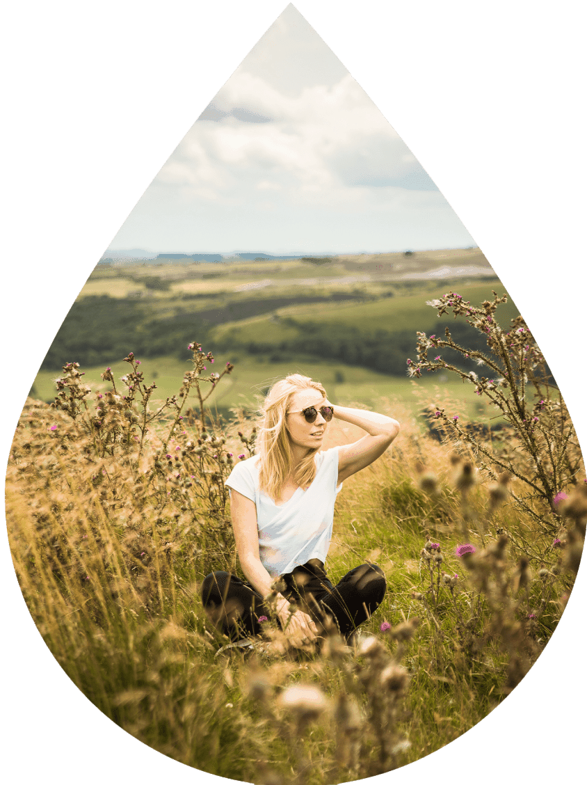 Blonde headed girl sitting in a field within an image shaped like a tear drop.